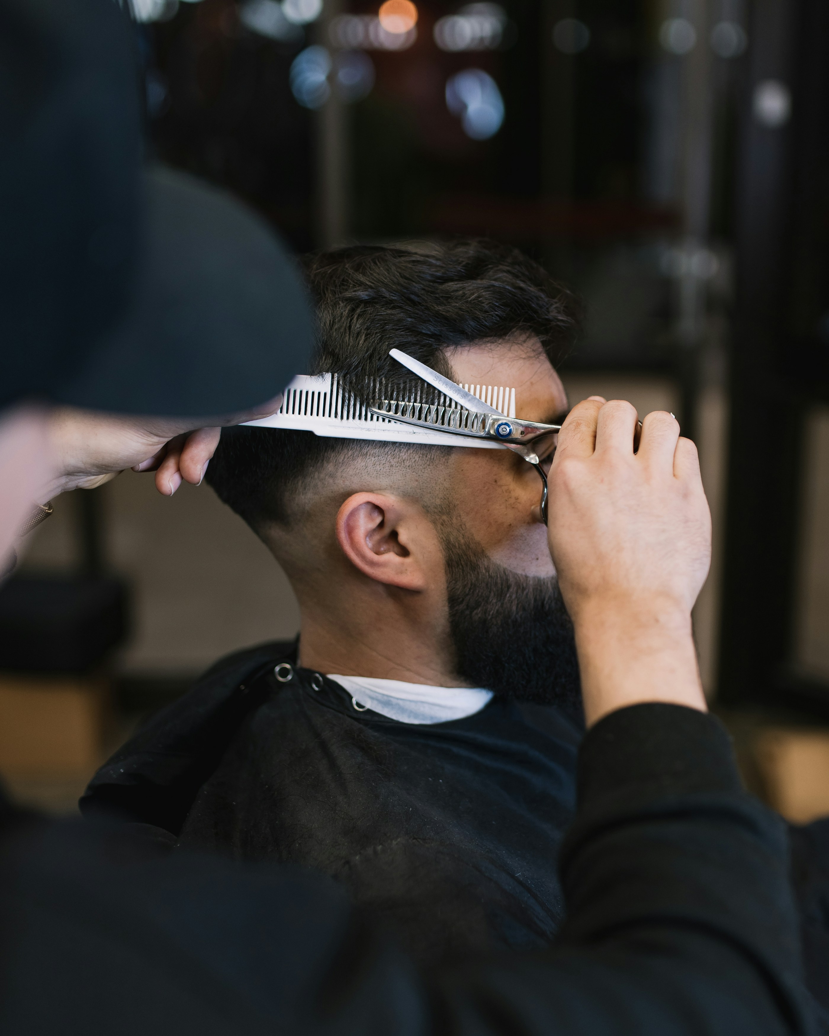 A barber carefully trimming a client's beard in a sleek, sophisticated barbershop.